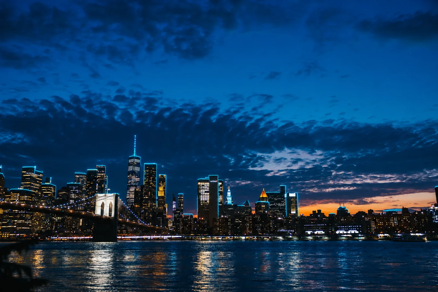 Lower Manhattan and Brooklyn Bridge illuminated beneath a blue evening sky